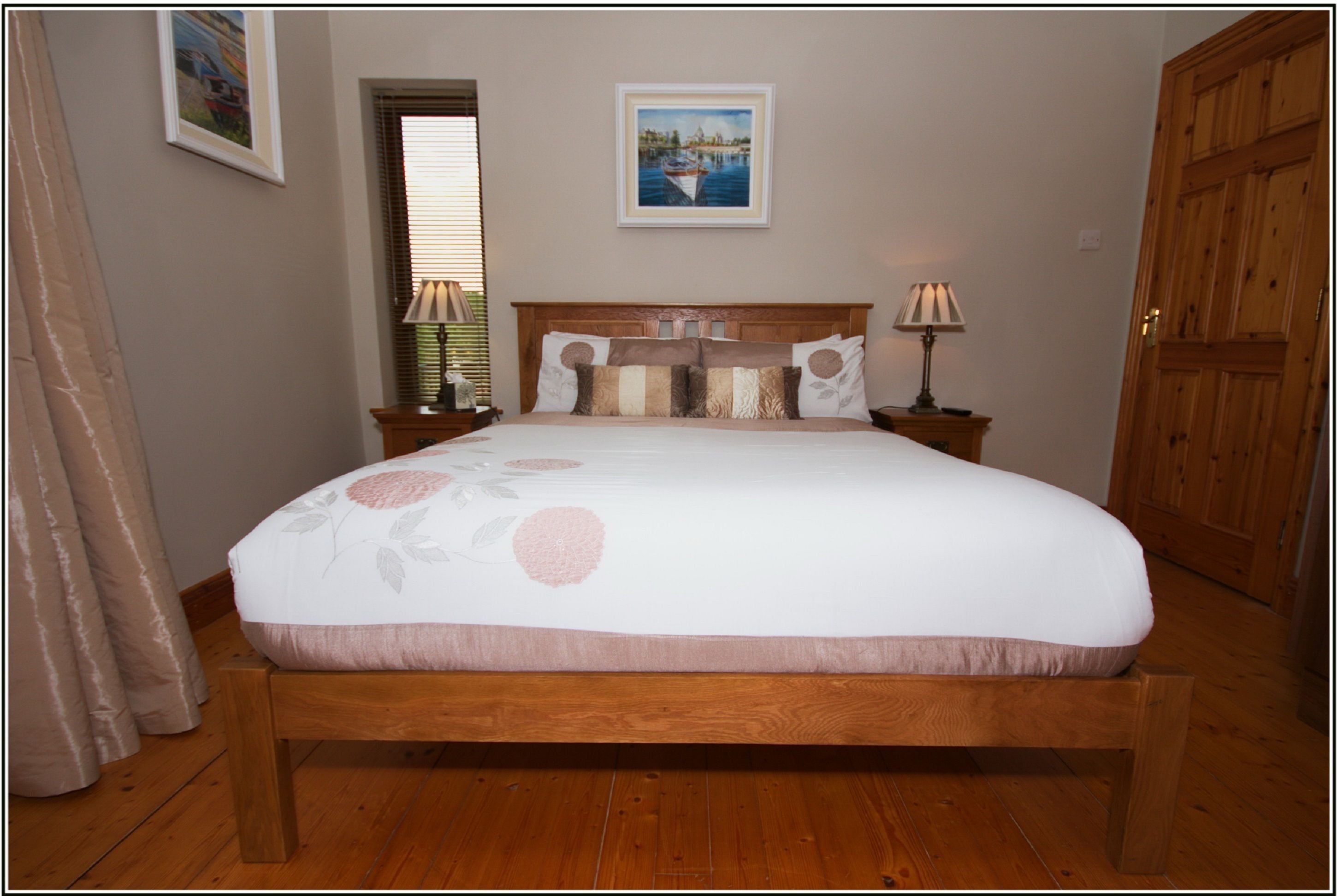 A bedroom with a wooden bed, two bedside tables, a nightstand, a window with blinds, and a door.