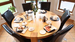 Une table de salle à manger ronde en bois, mise pour un repas, avec différents plats, notamment une assiette de nourriture, une théière, des tasses et un vase rempli de fleurs.