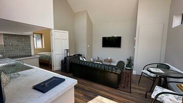 Ett kompakt bostadsutrymme med ett litet kök, en soffa, en matplats och en TV som är monterad på väggen.