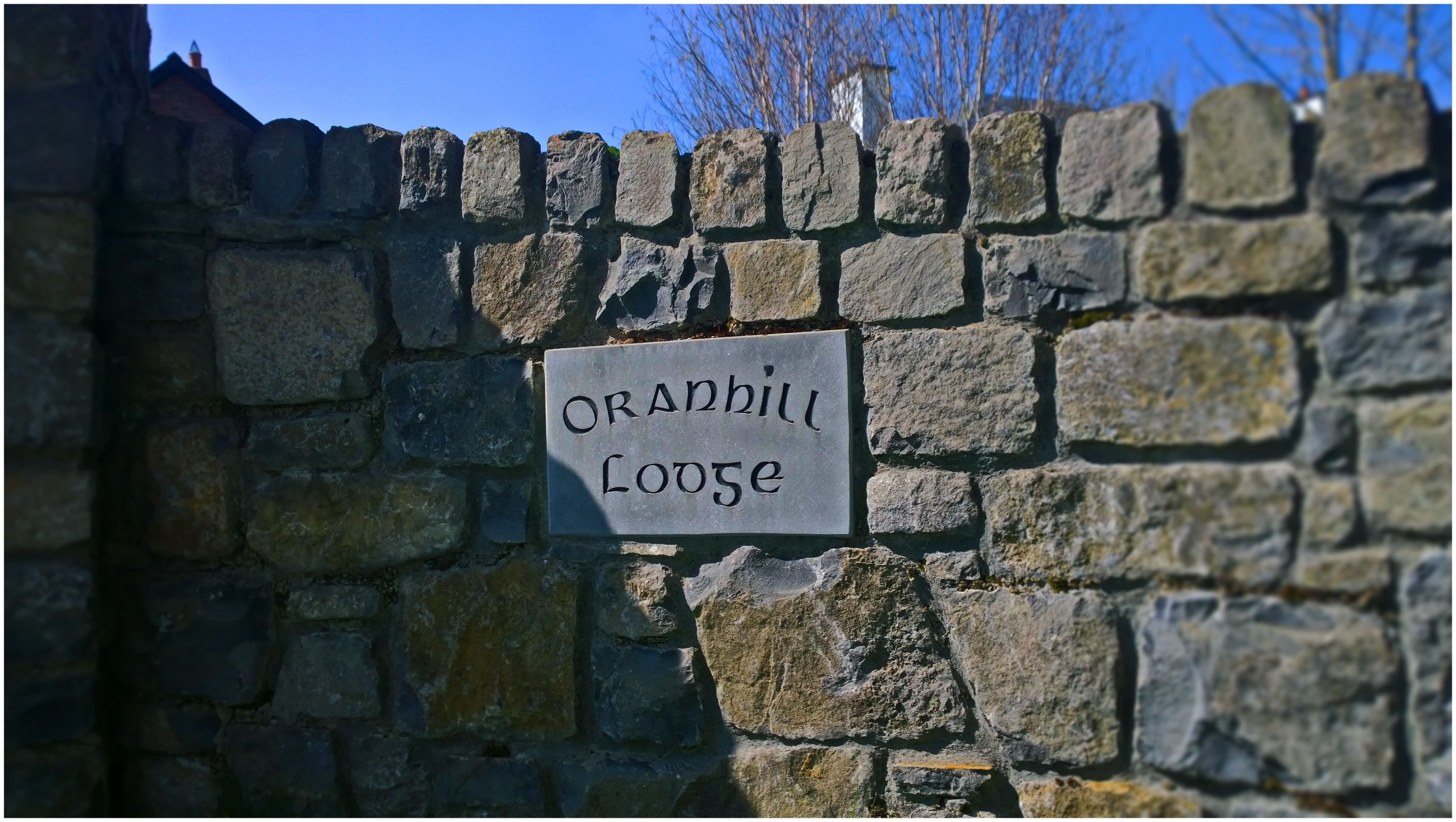 A stone wall with a sign that reads "Oranhill Lodge".