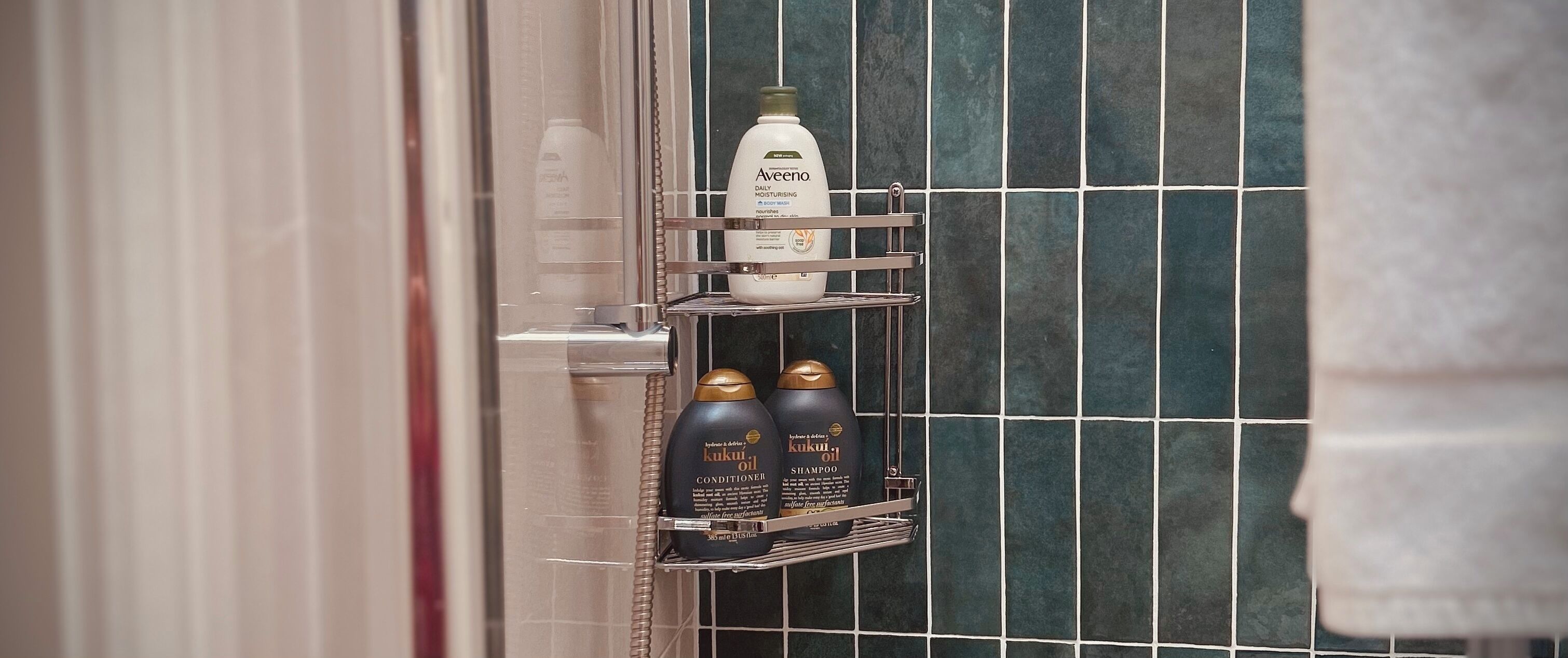 Un baño con pared de azulejos, un perchero y un estante con artículos de aseo.