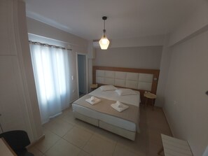 Un dormitori amb un llit gran, una taula de nit, una làmpada penjant i una porta que dona a una altra habitació.
