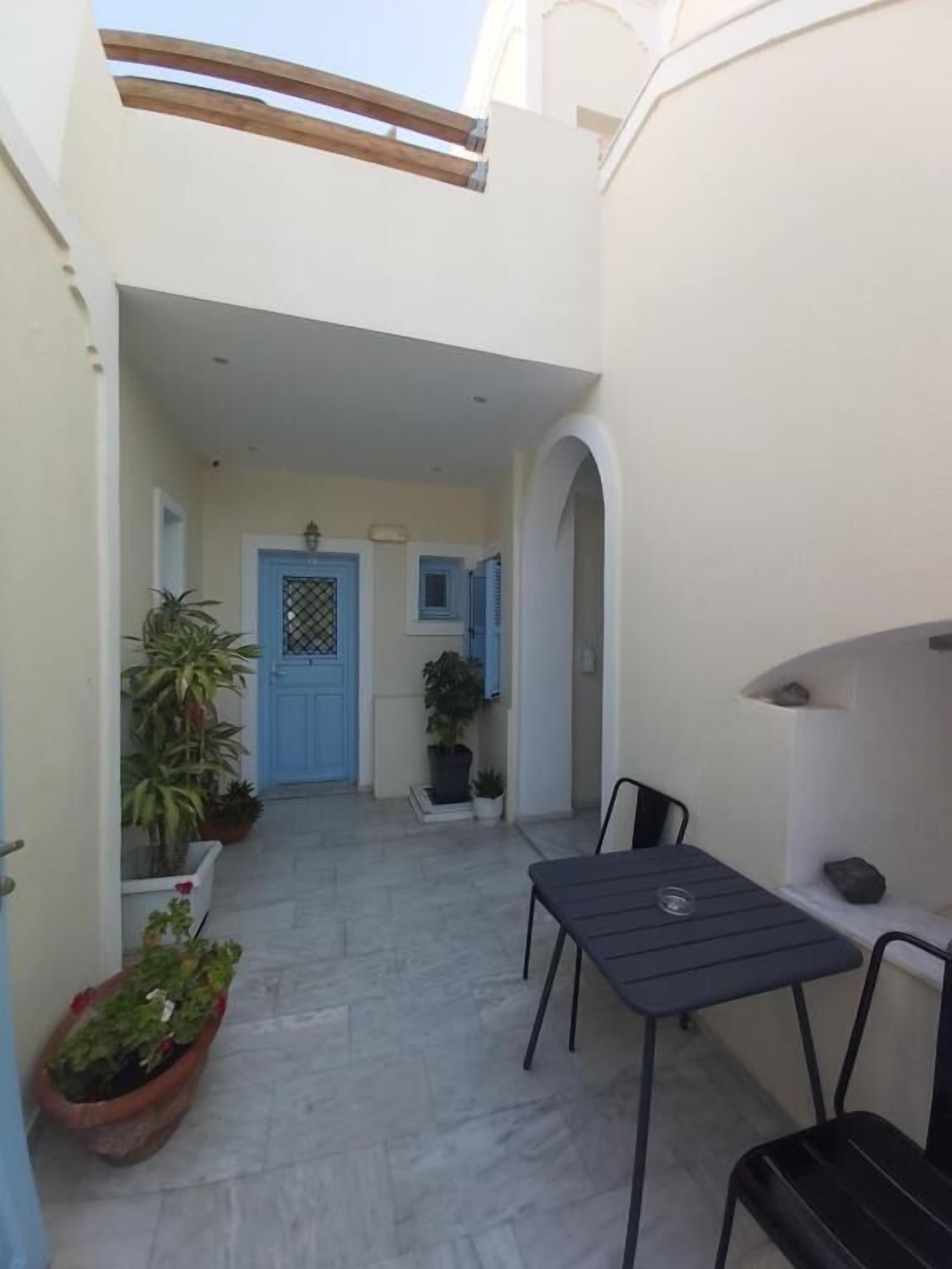 A narrow courtyard with a blue door, potted plants, and a table with chairs.