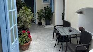 Un espacio al aire libre con patio, mesa, sillas, plantas en macetas y una puerta azul.