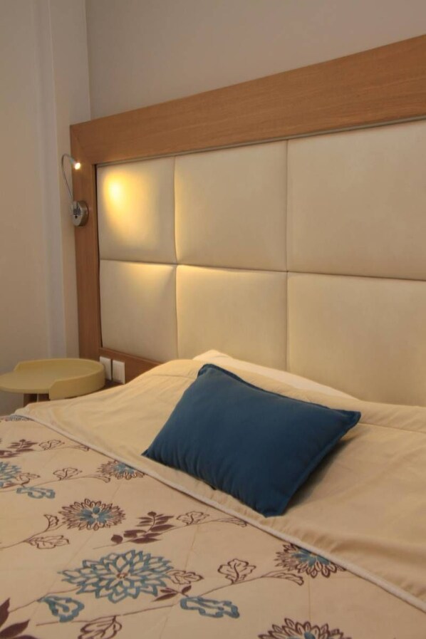 A hotel room with a bed, a bedside table, and a headboard with built-in lighting.