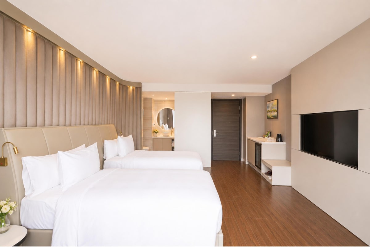 A hotel room with two beds, a TV, a mirror, a small table, and a door leading to another room.