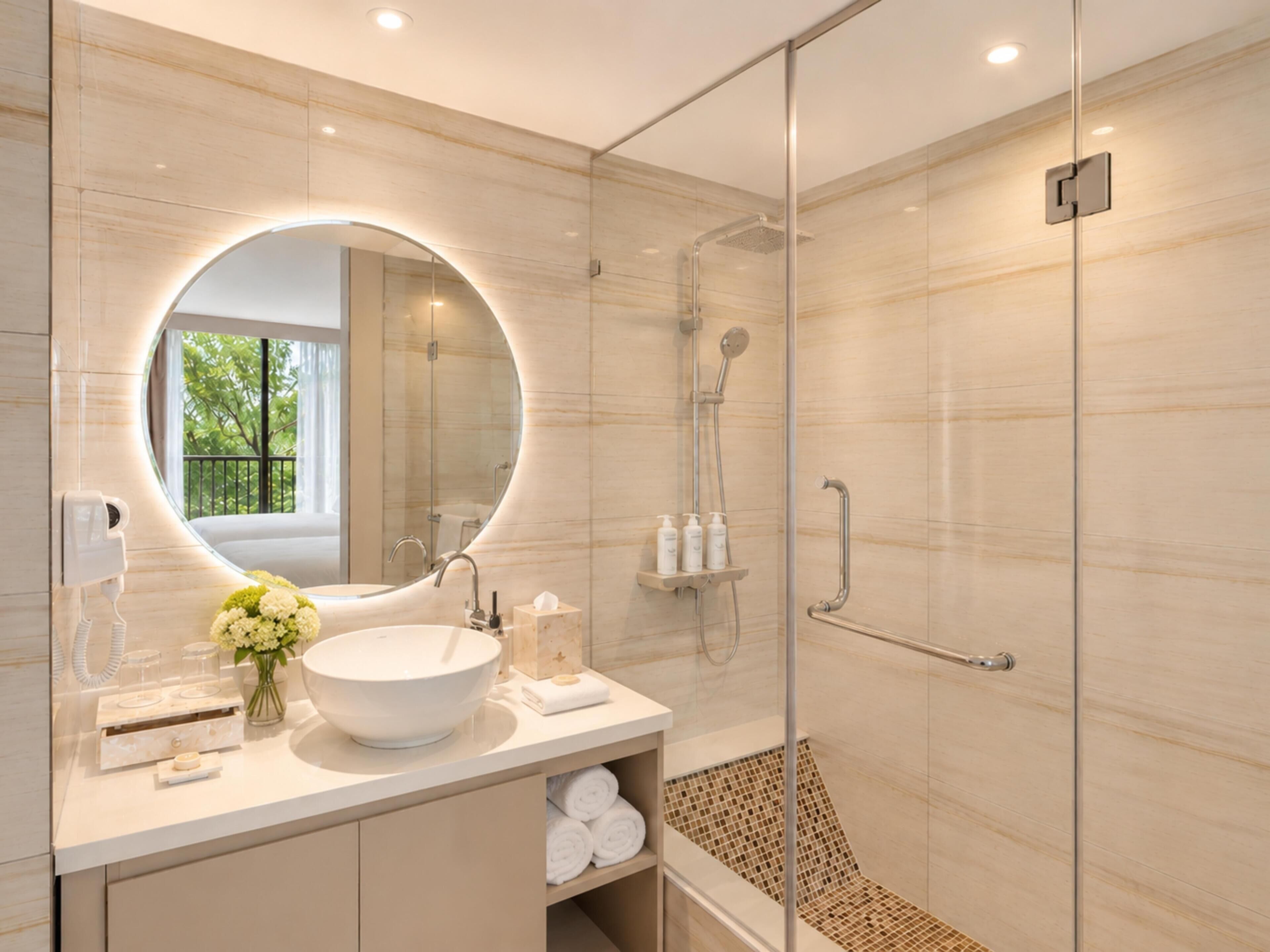 A modern bathroom with a round mirror, a large sink, a shower, and a bench.
