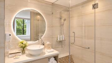 A modern bathroom with a round mirror, a large sink, a shower, and a bench.