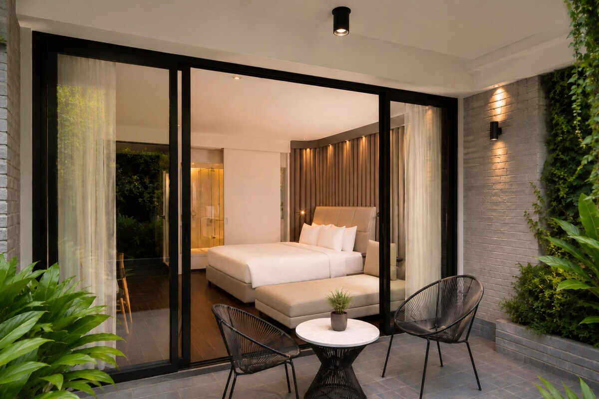 A modern hotel room with a large bed, a glass door leading to a balcony, and a small table with two chairs.
