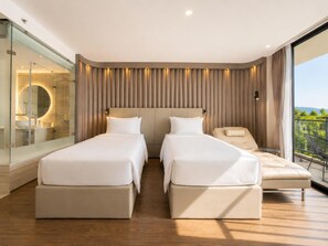 Una habitación de hotel moderna con dos camas, un baño con paredes de vidrio, un balcón con vistas y un ventanal grande.