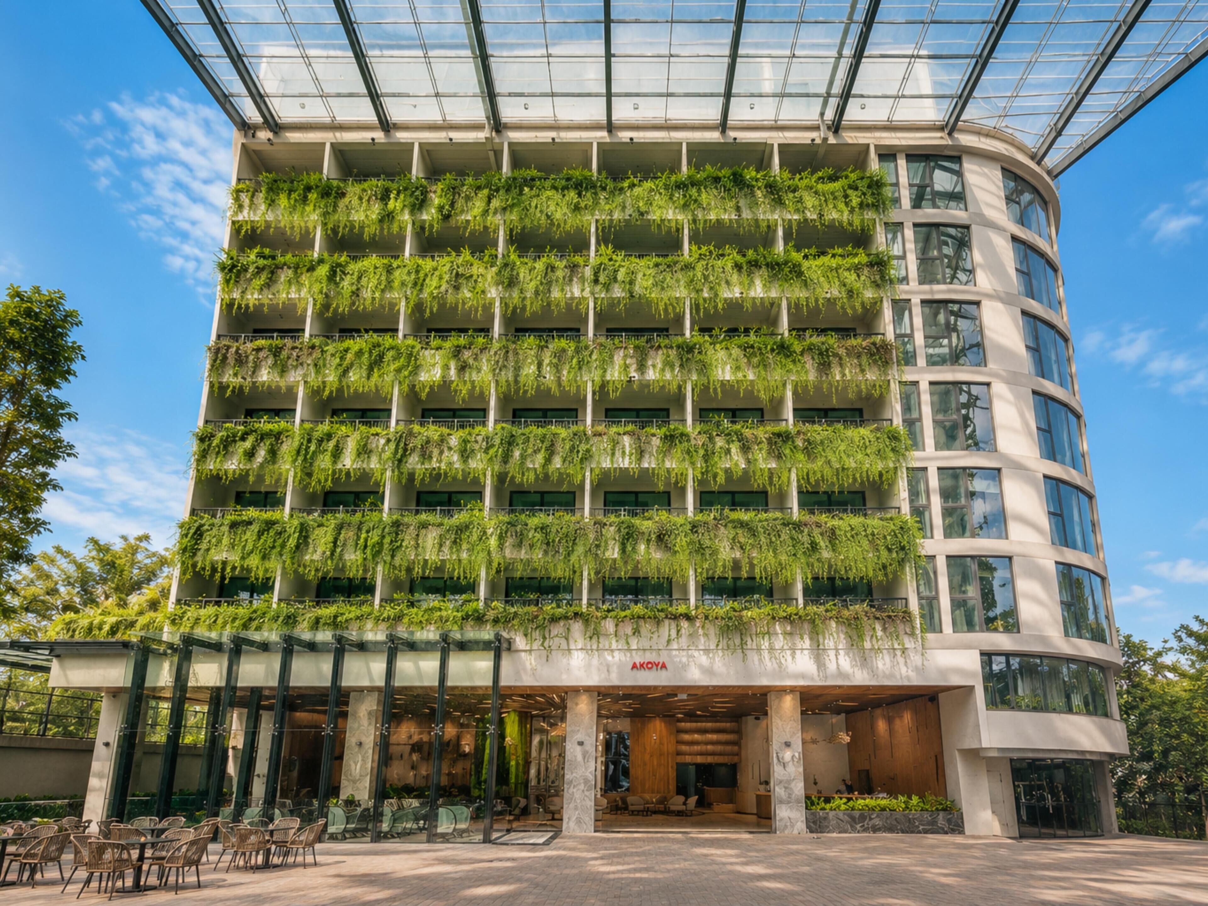 A multi-story building with a glass facade, green plants on the exterior, and a visible entrance with outdoor seating.