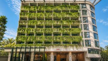 A multi-story building with a glass facade, green plants on the exterior, and a visible entrance with outdoor seating.