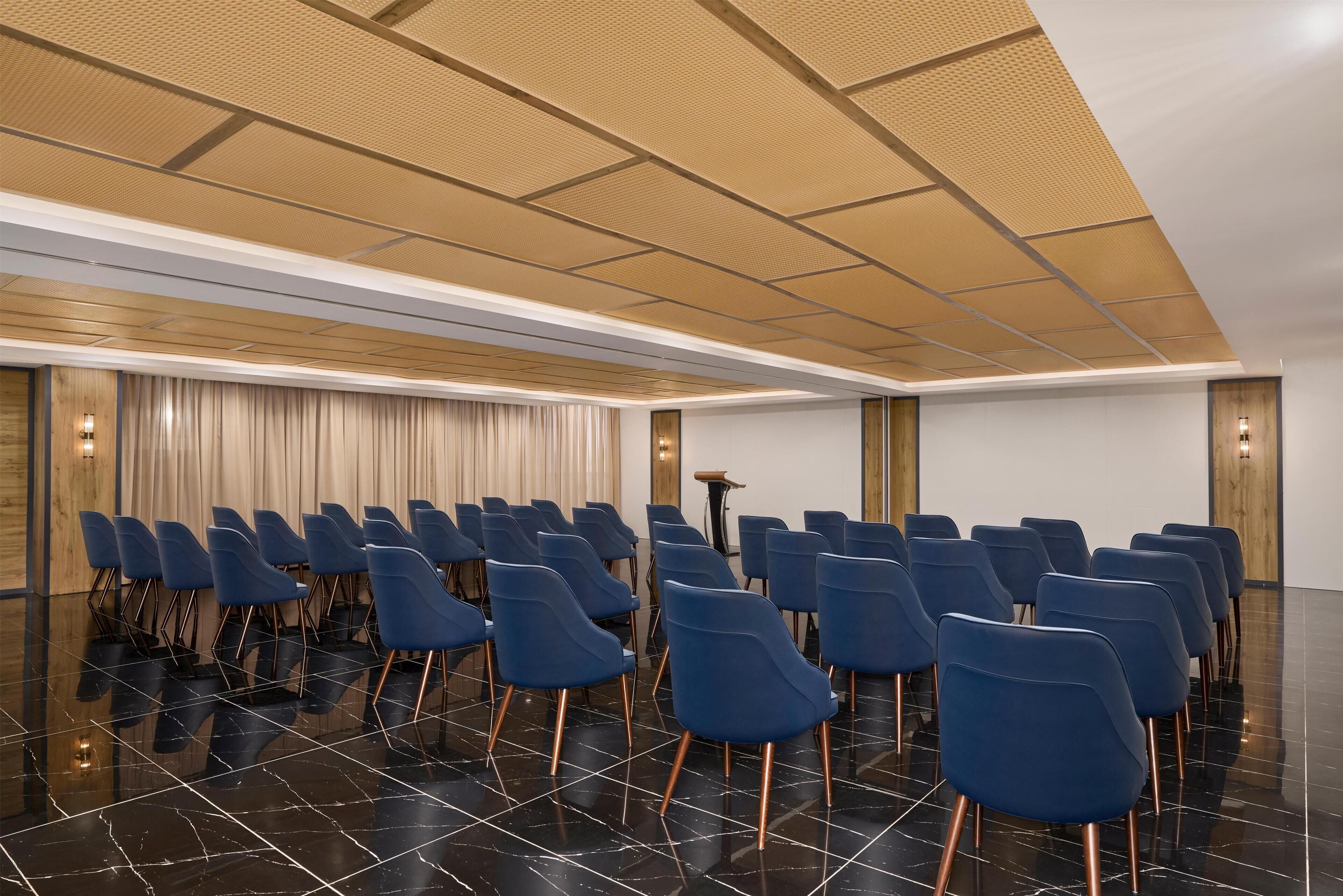 A conference room with rows of blue chairs, a podium, and a wooden ceiling.