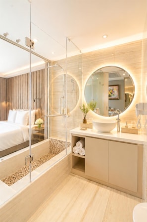 A modern bathroom with a glass-enclosed shower, a round mirror, a white sink, and a wooden vanity.