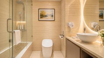 A modern bathroom with a glass shower enclosure, a toilet, a sink with a large mirror, and a framed landscape painting on the wall.