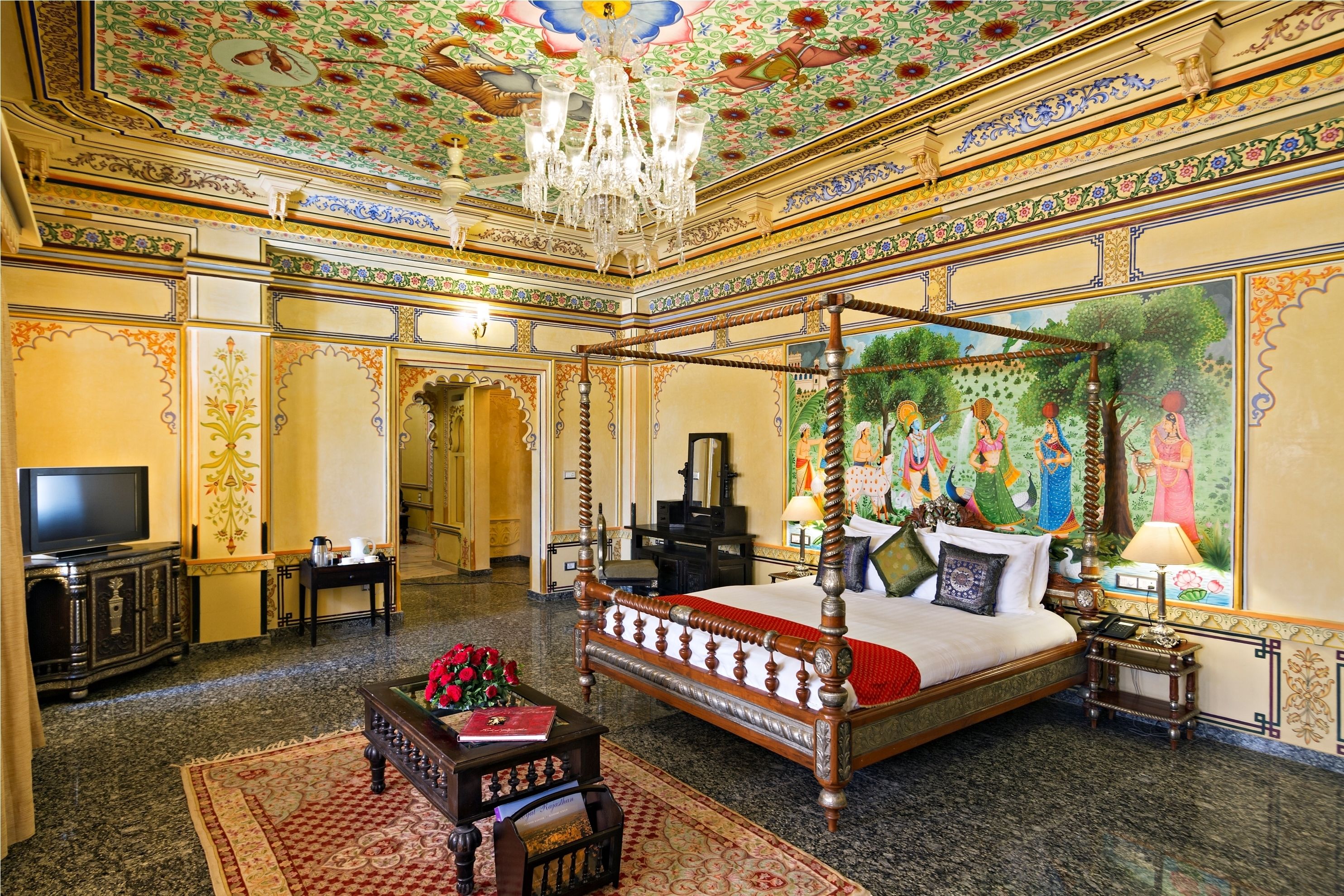 A luxurious bedroom with a four-poster bed, a chandelier, and a mural on the wall.