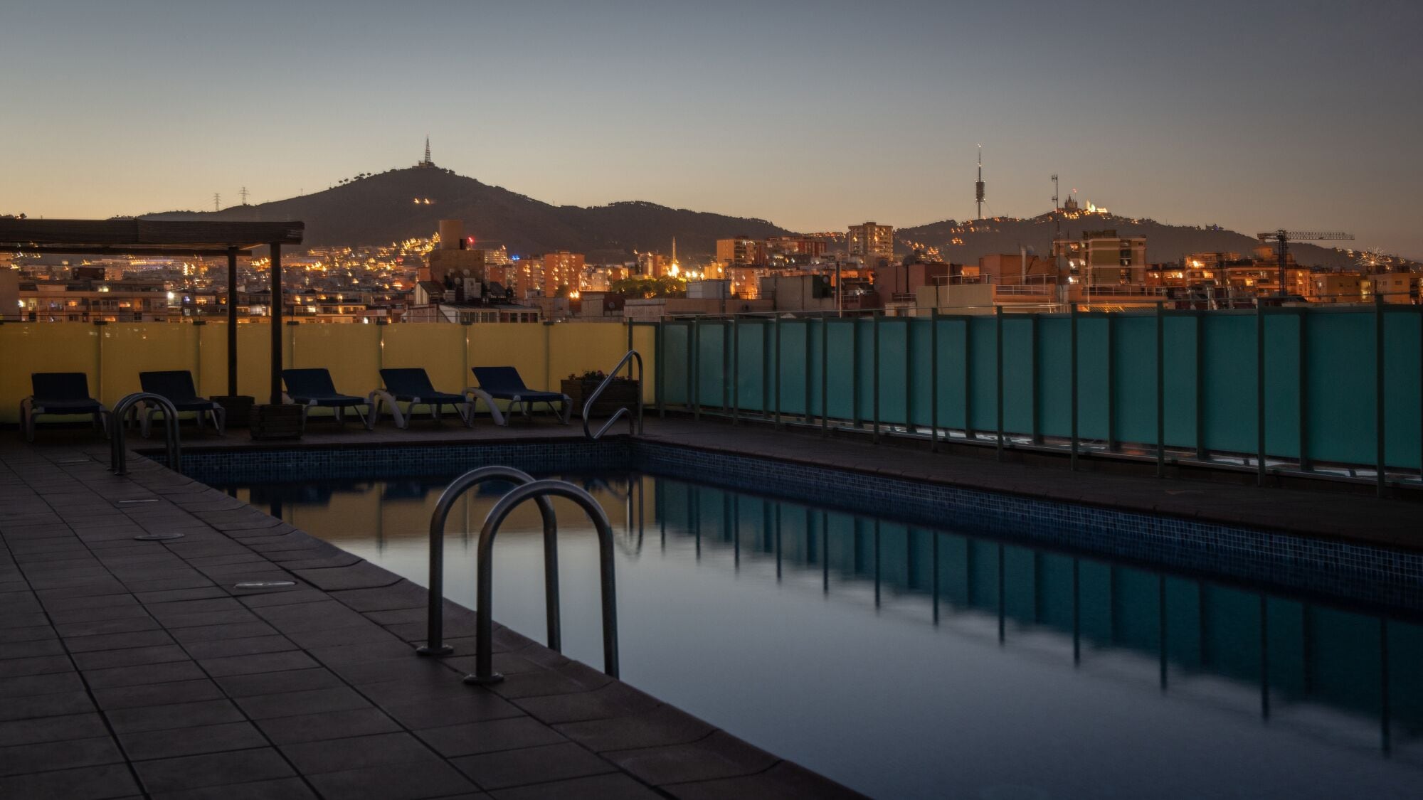 A rooftop pool with a cityscape view at dusk.