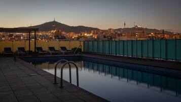 A rooftop pool with a cityscape view at dusk.