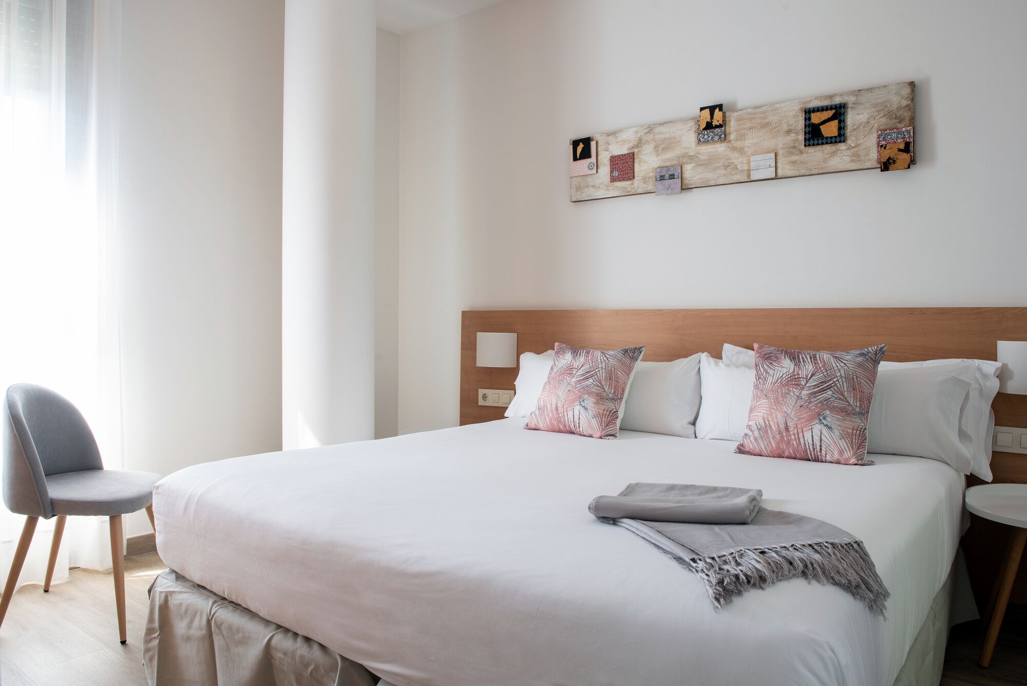 Une chambre d’hôtel avec un grand lit, une tête de lit en bois, une table de chevet, une chaise et une œuvre d’art murale.
