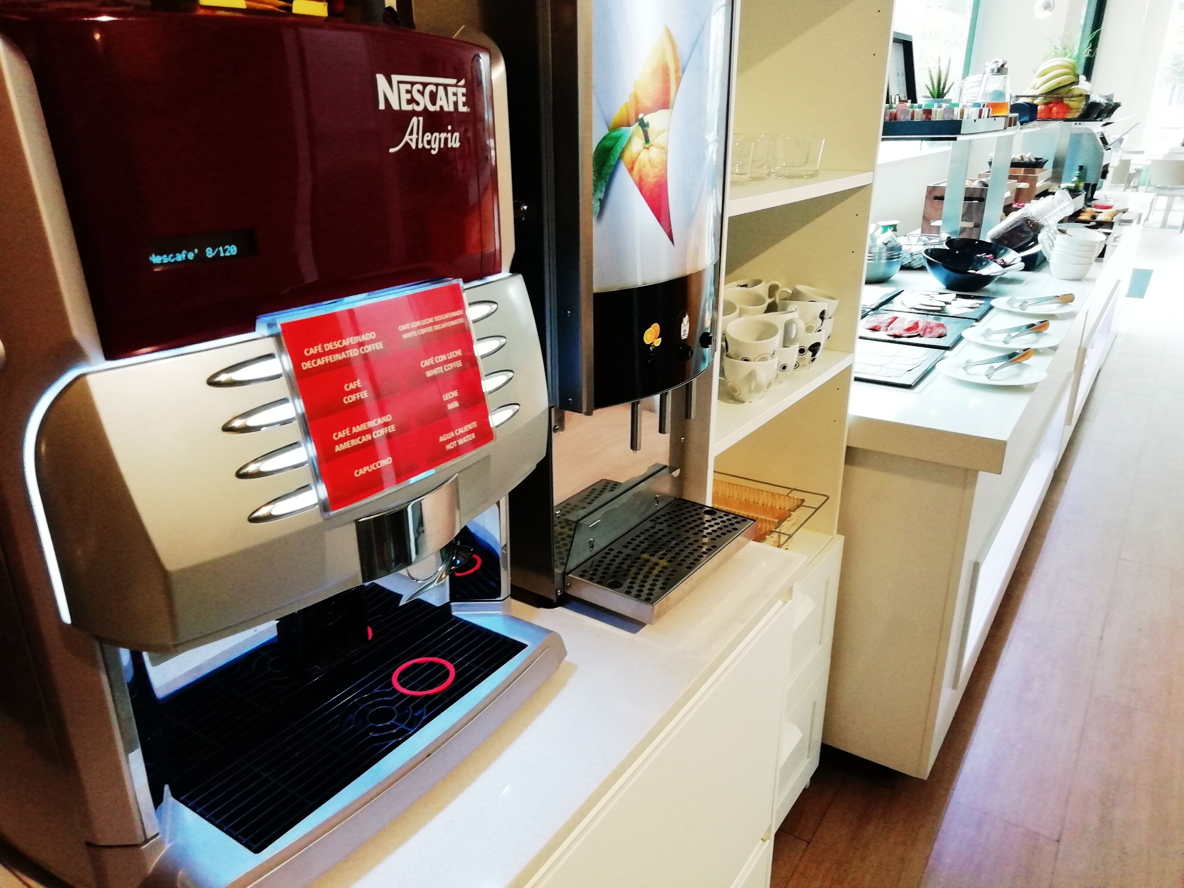 Una máquina de café Nescafé con pantalla digital, un tablero de menú y una estación de café con tazas y utensilios.
