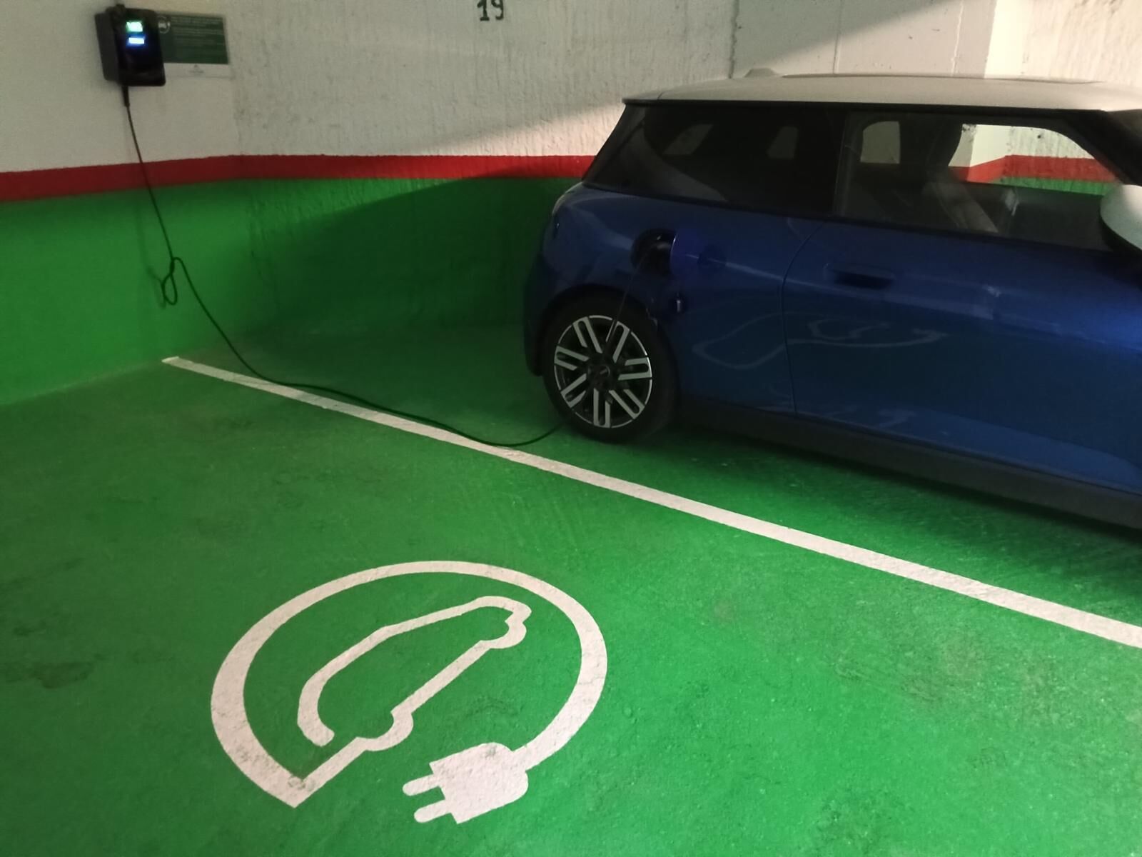 Un espacio de estacionamiento con piso verde y un símbolo blanco para cargar vehículos eléctricos.
