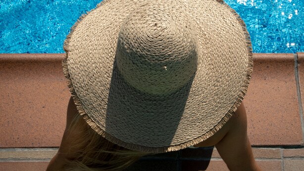 Une personne portant un chapeau de paille, près d’une piscine.