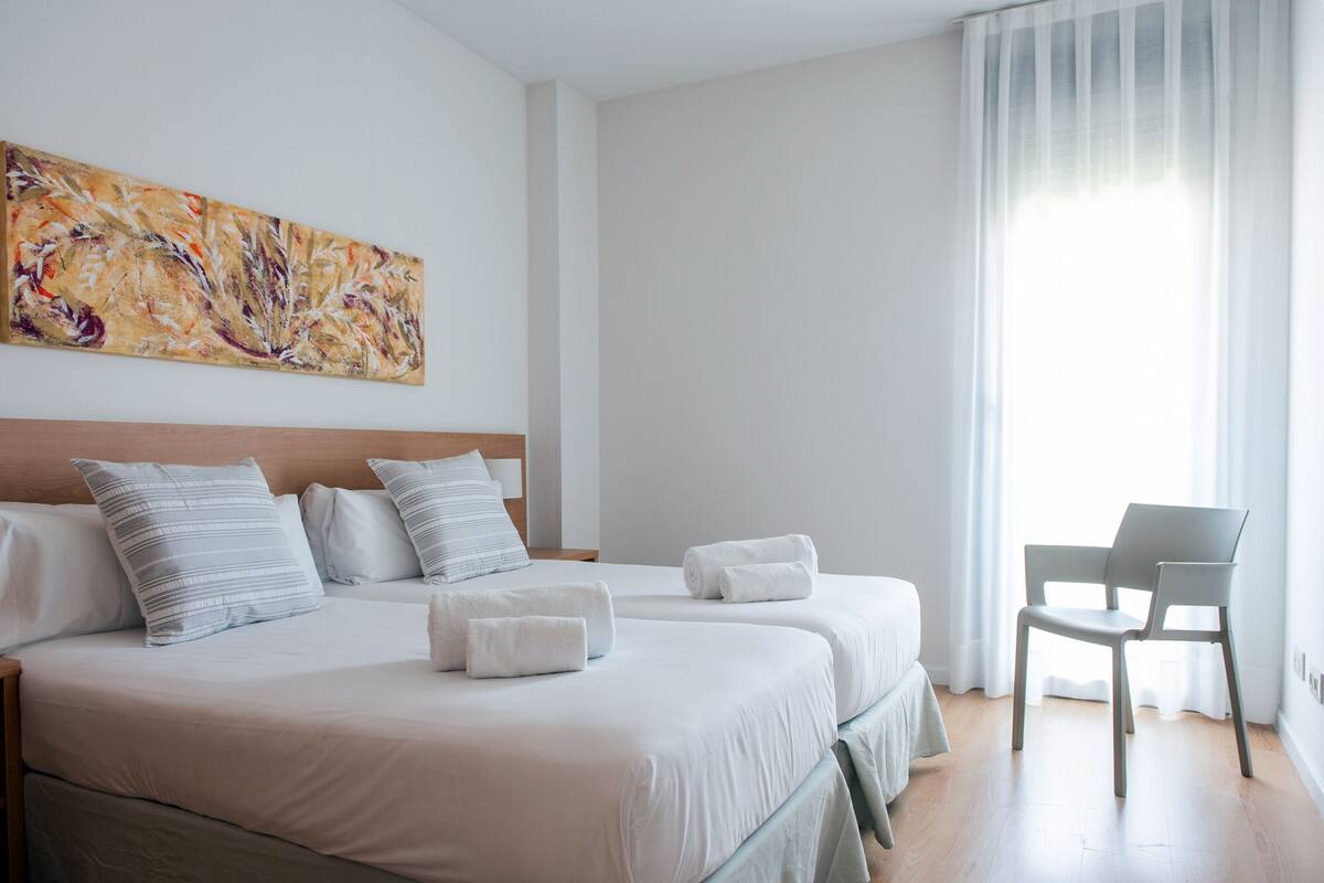 Een hotelkamer met twee bedden, een stoel en een schilderij aan de muur.