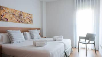 A hotel room with two beds, a chair, and a painting on the wall.