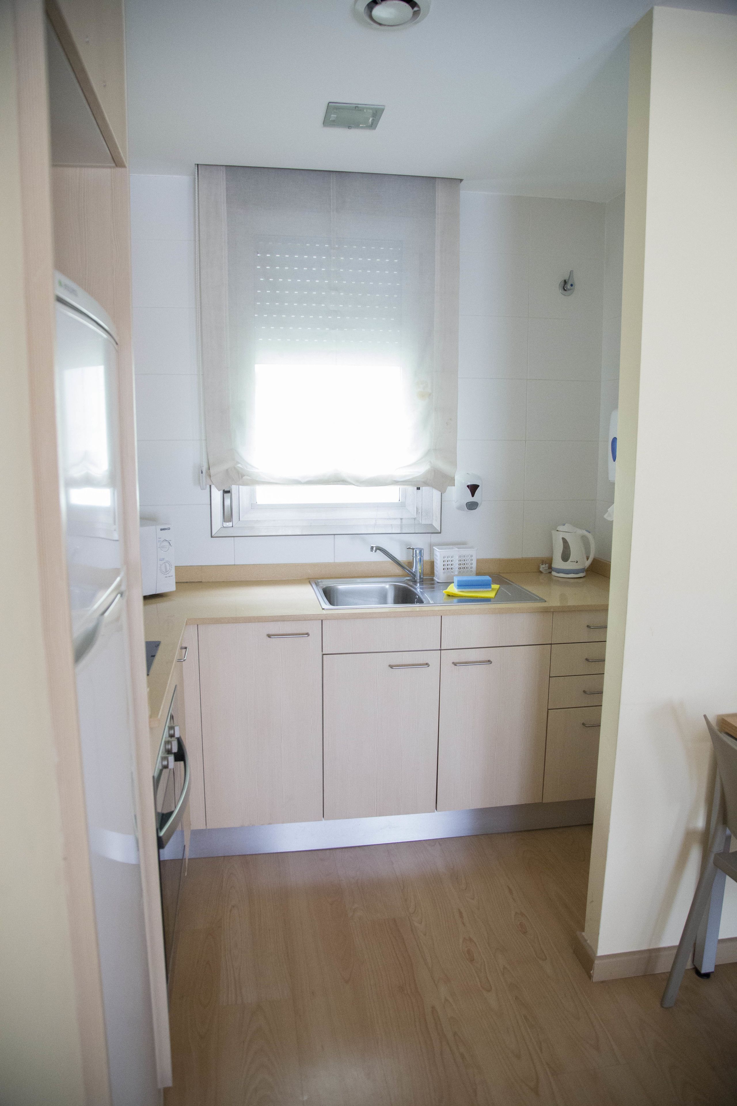 Een keuken met houten kastjes, een roestvrijstalen spoelbak en een raam met zonwering.