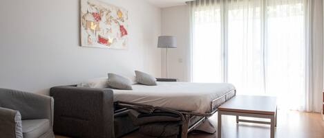 A modern bedroom with a bed, a sofa, a small table, and a lamp.