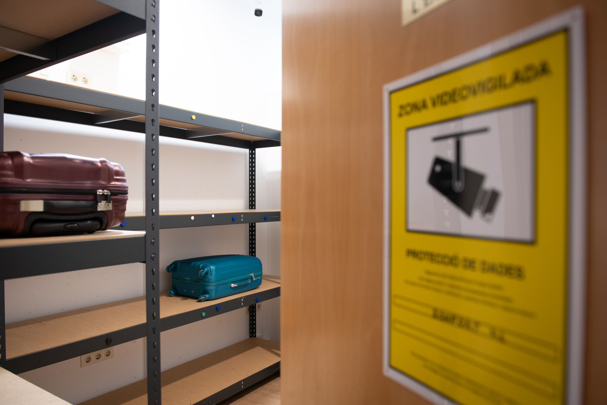 A storage area with metal shelves, a wooden door, and a yellow sign with a black and white warning symbol.