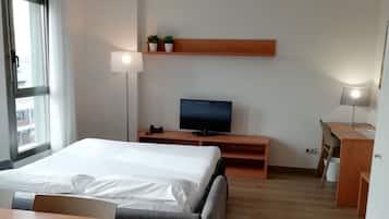 Een hotelkamer met een bed, een bureau, een televisie, een lamp en een klein plankje met planten.