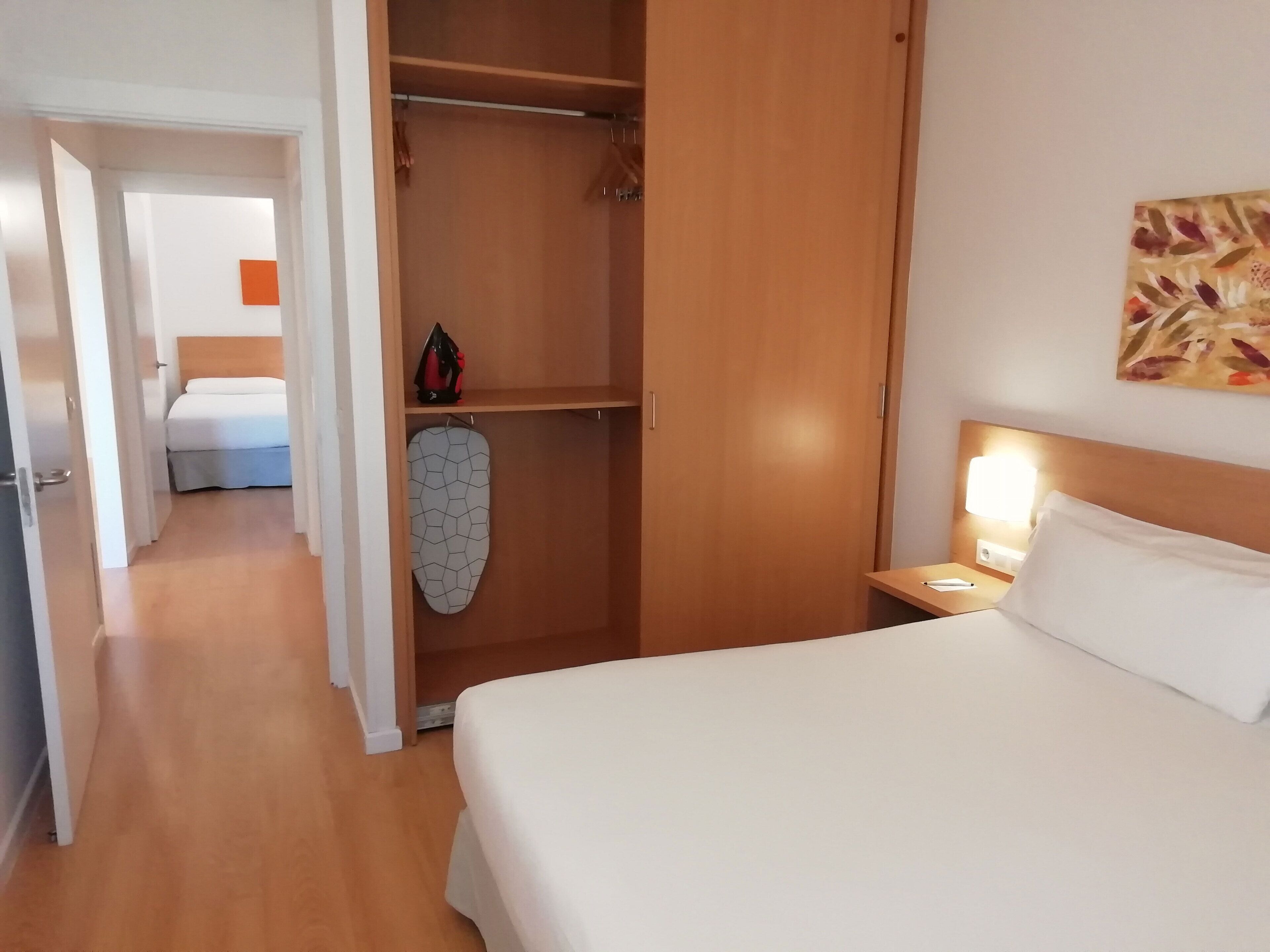 Una habitación de hotel con una cama, un armario y una mesita de noche con lámpara.
