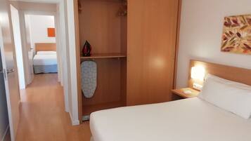 Una habitación de hotel con una cama, un armario y una mesita de noche con lámpara.
