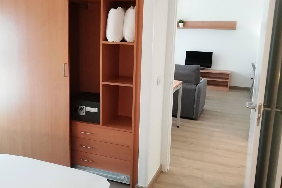 Een hotelkamer met een houten kledingkast, een bed, een bureau met stoel en een televisie.
