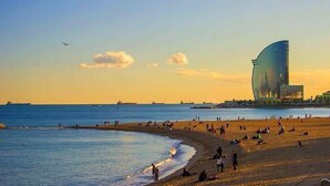 Une plage avec des gens, un bâtiment aux lignes courbes et un ciel dégagé.