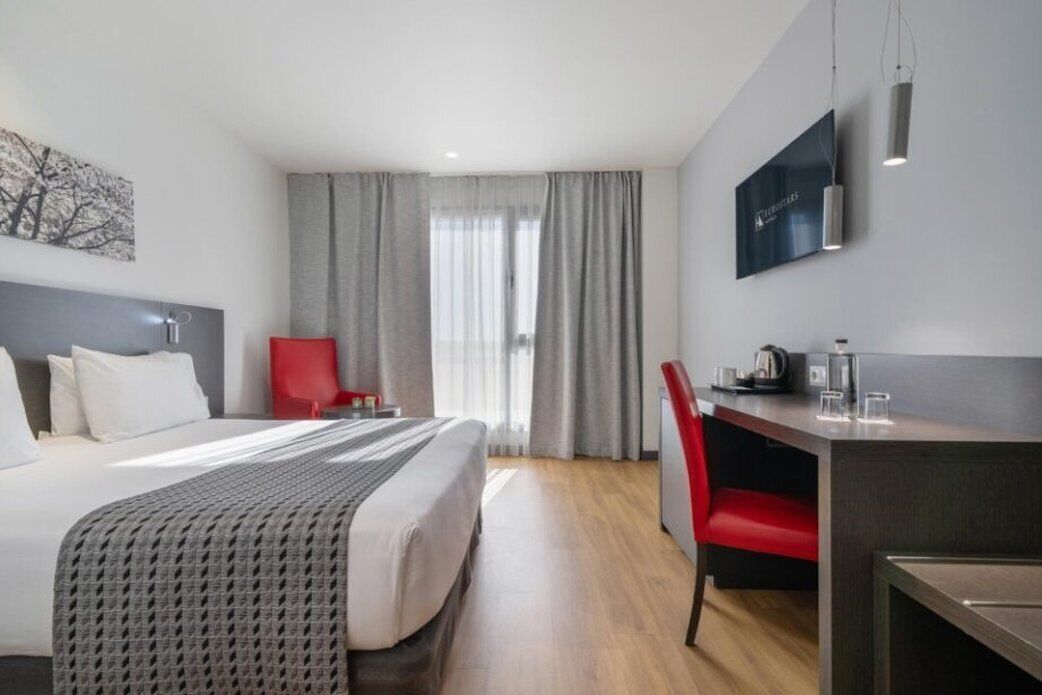 Une chambre d’hôtel avec un lit, un bureau, une chaise, une télévision et une fenêtre avec des rideaux.