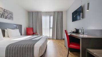 Une chambre d’hôtel avec un lit, un bureau, une chaise, une télévision et une fenêtre avec des rideaux.