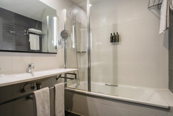 Une salle de bain moderne avec une douche à parois de verre, une baignoire blanche et un meuble-lavabo doté d’un miroir et d’un porte-serviettes.