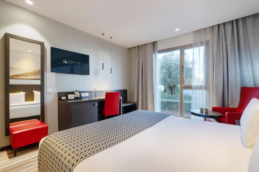 Habitación de hotel con una cama grande, un escritorio, una silla y un televisor en la pared.