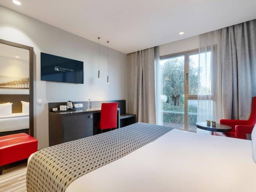Habitación de hotel con una cama grande, un escritorio, una silla y un televisor en la pared.