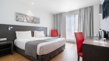 A hotel room with a bed, a desk, a chair, a TV, and a window with curtains.