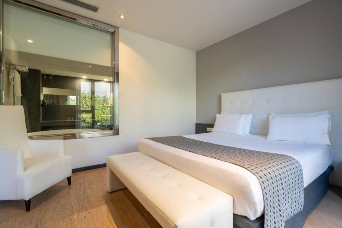Een moderne slaapkamer met een groot bed, een bankje, een stoel en een groot raam.