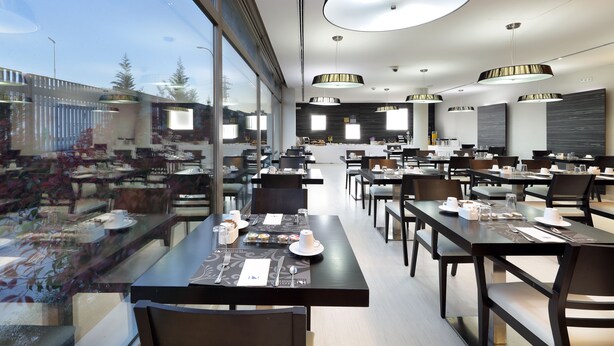 Een moderne eetruimte met meerdere tafels en stoelen, grote ramen en moderne verlichtingsarmaturen.