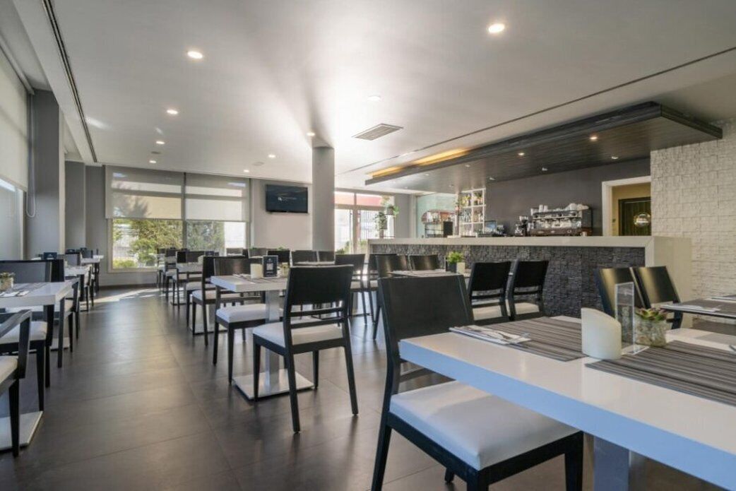 A modern restaurant with a long counter, black chairs, and a stone wall backdrop.