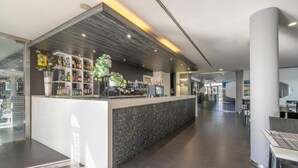 Een moderne bar met een stenen toonbank, flessenkasten en een potplant.