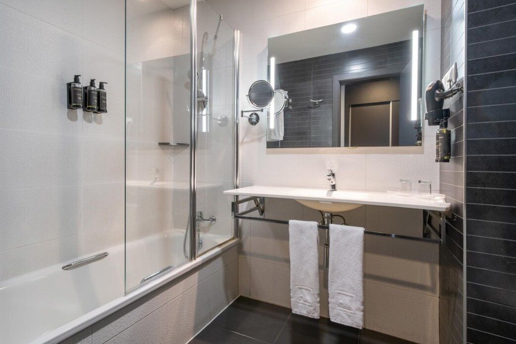 A modern bathroom with a glass-enclosed shower, a white sink, and a large mirror.