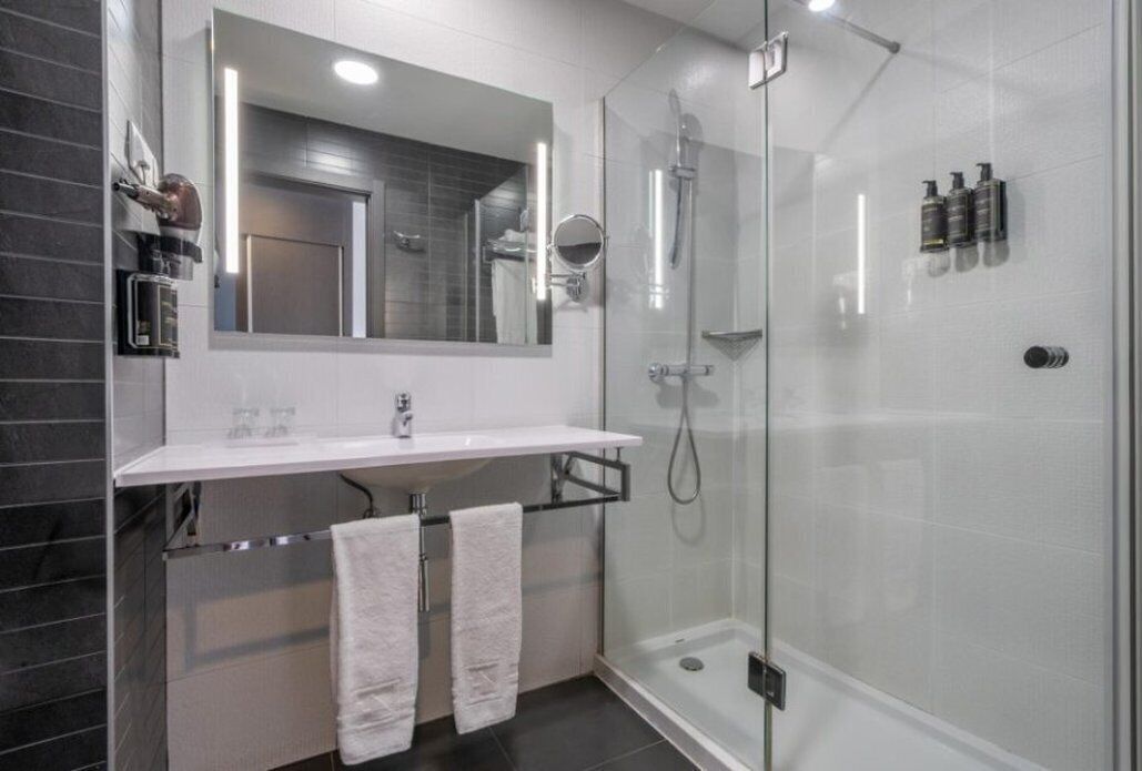 A modern bathroom with a glass-enclosed shower, a large mirror, and a white countertop.