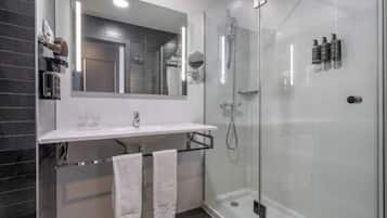 A modern bathroom with a glass-enclosed shower, a large mirror, and a white countertop.