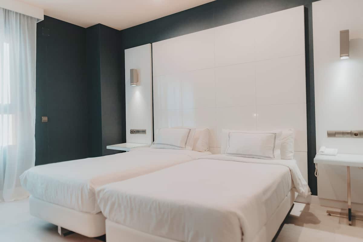 A modern hotel room with two beds, a large mirror, a bedside table, and a small desk with a telephone.